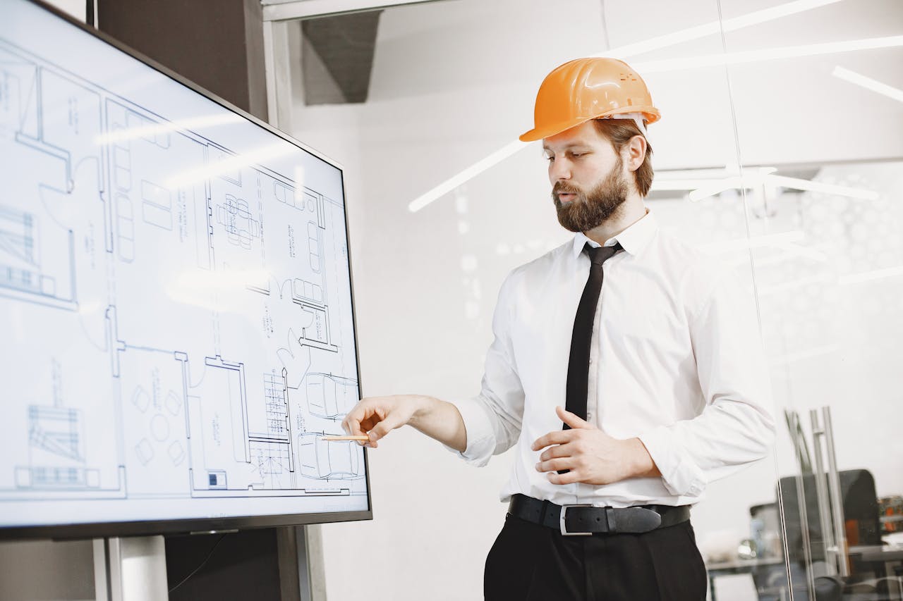 home-services-01 Architect in hard hat reviewing blueprints on a screen, discussing plans in modern office.